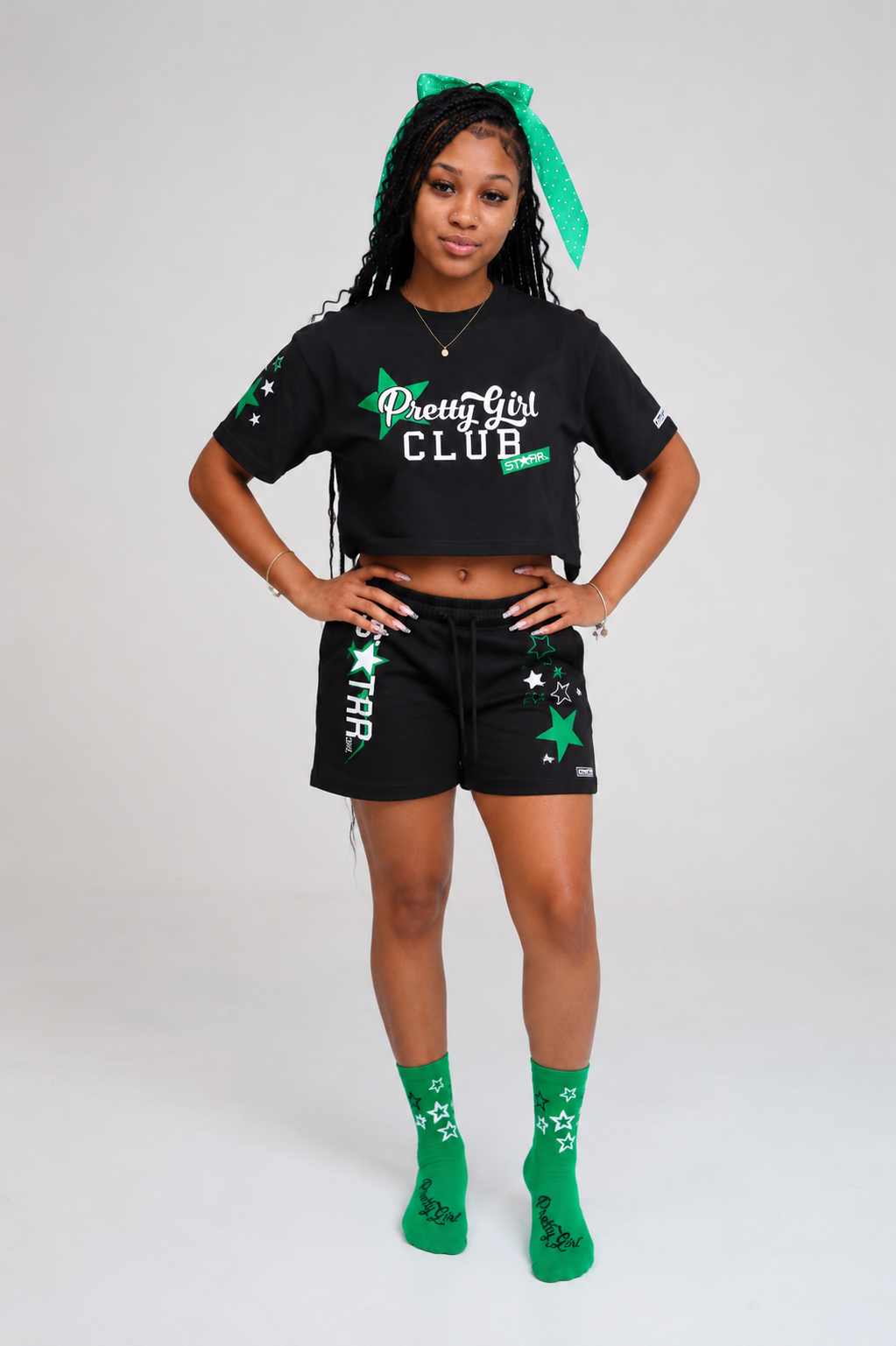 Starr Girls Pretty Girl Club short sleeve crop top in black and green, shown on a white and green lifestyle background.